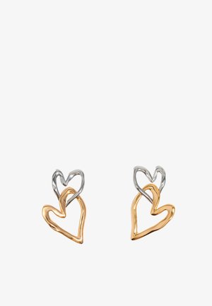 Pendientes en forma de corazón de oro y plata con diseños entrelazados. Presentan superficies lisas y pulidas con acabados metálicos diversos.