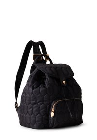 Black quilted backpack with a rounded body, honeycomb texture, front zip pocket, and adjustable logo strap. Features a top flap and gold hardware.