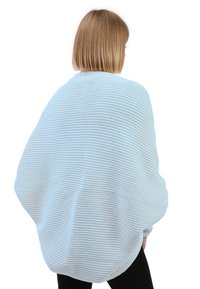Helles blaues, übergroßes Strickpullover mit einem strukturierten, gerippten Design und runder Form, getragen über schwarzen Hosen.