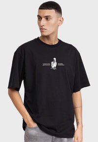 Zwart katoenen T-shirt met korte mouwen, voorzien van een witte afbeelding van een haan en de tekst "WAKE UP CALL FOR THE BRAVE DREAMER DEPARTMENT."