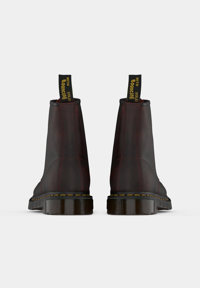 Bottines en cuir rouge foncé et noir avec surpiqûres jaunes. Elles présentent un design haut et arrondi ainsi que des boucles de traction pour un enfilage facile.