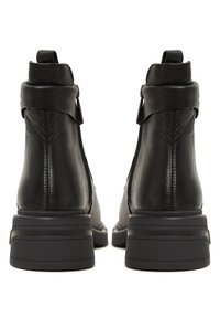 Bottines en cuir noir avec fermeture éclair, bout rond et semelle épaisse texturée. Détail de couture à l'arrière et design de talon superposé.
