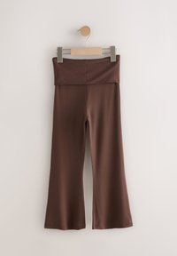 Leggings marron évasés en tissu doux et extensible avec une taille large, suspendus à une pince en bois sur un présentoir minimaliste.