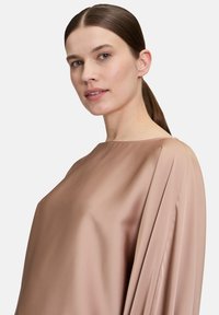 Satinbluse in einem gedeckten Beigeton, mit lockerem Schnitt, drapierten Ärmeln und glatter Textur sowie hohem Kragen.