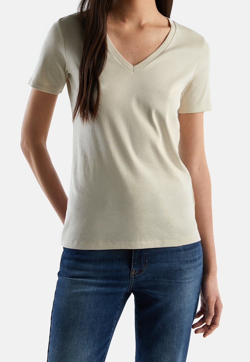 V-ringad, kortärmad t-shirt i ljus beige, tillverkad av mjuk bomull. Har en figurnära design och slät textur. Matchad med blå jeans.