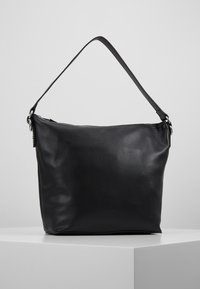 Svart axelväska i läder med texturerad yta, kurvad form och en smal band. Har dragkedjeförslutning och minimal märkning.