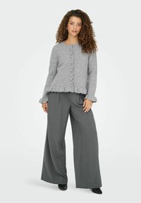 Cardigan en tricot gris avec bordure en volants et fermeture à boutons, associé à un pantalon gris à jambe large. Texture lisse, design décontracté.