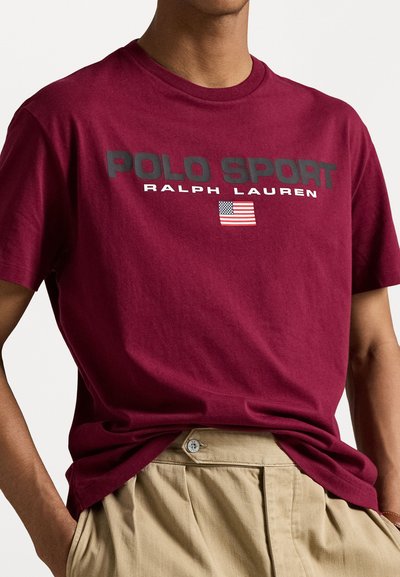Bordová bavlnená tričko s potlačou "POLO SPORT" a "RALPH LAUREN" v čiernej farbe. Detail americkej vlajky pod textom. Bežný strih.