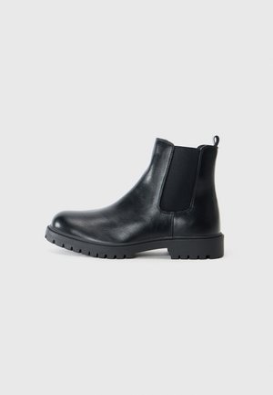 Las botas Chelsea de cuero negro cuentan con paneles laterales elásticos, puntera redondeada y suela de goma con tracción. Diseño minimalista con una lengüeta.