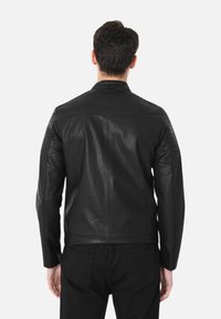 Giubbotto di pelle nera con dettagli trapuntati sulle spalle e una finitura liscia. Caratterizzato da un colletto alzato e un design slim-fit.