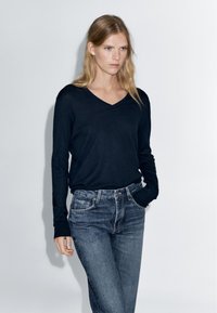 Black long-sleeve V-neck sweater paired with faded blue jeans. Soft texture, fitted silhouette, and simple design without patterns or embellishments.