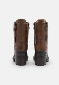 Brune skinnankelsko med teksturert overflate, med glidelås på siden, fôr av pels og en solid svart hæl med preget merkevare.