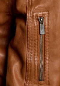 Braune Lederjacke mit einem Metallreißverschluss auf der Vorderseite, strukturiertem Bezug und detaillierten Nähten entlang der Schultern.