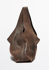 Brązowa skórzana torba o unikalnym kształcie i fakturze, charakteryzująca się luźnym fasonem i górnym otwarciem podkreślonym wycięciem.