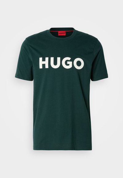 Тъмнозелена памучна тениска с голямо бяло лого "HUGO" на предната част. Класически кръгъл врат и къси ръкави. Гладка текстура.
