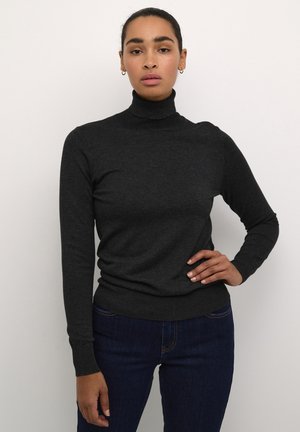 Pull encolure montant gris foncé en matière tricotée douce, avec des manches longues et une silhouette ajustée, associé à un jean bleu foncé.