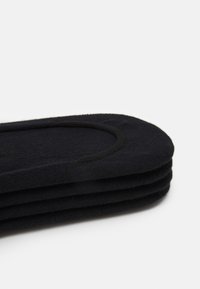 Svarta tyginsoles staplade, med en slät textur och oval form. Rundade kanter med en subtil sydd kant för extra detalj.