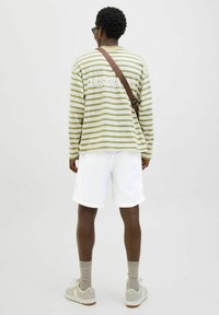 Camisa de rayas olive y blanca de manga larga con el texto "ORIGINAL", combinada con pantalones cortos blancos y zapatillas beige, vista desde la parte de atrás.
