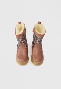 Botas de inverno para crianças com biqueira de couro castanho, parte superior em tecido floral, fechos de correr nas laterais e forro em lã cremosa por dentro.