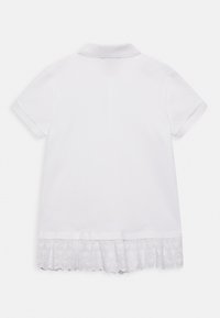 Abito polo bianco con maniche corte, caratterizzato da un bordo in pizzo all'orlo. Il pizzo presenta un motivo floreale e bordi ondulati.