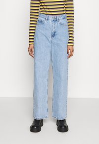 Ljust blå högmidjade denimjeans med avslappnad vida benpassform, utrustade med fem fickor och knäppning, matchade med svarta kraftiga stövlar.