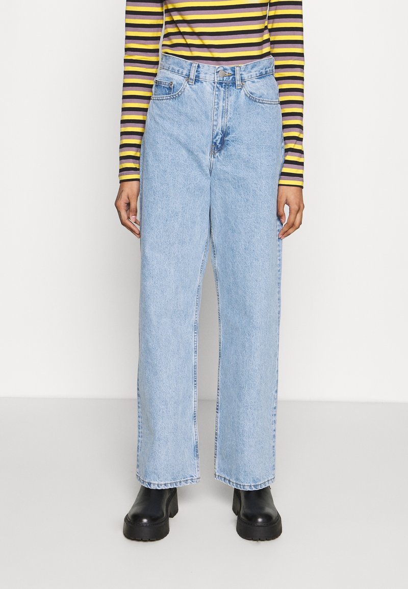 Ljust blå högmidjade denimjeans med avslappnad vida benpassform, utrustade med fem fickor och knäppning, matchade med svarta kraftiga stövlar.