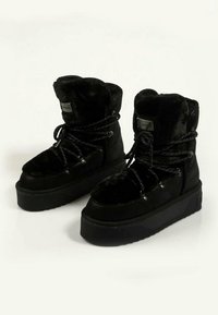 Botas de tobillo forradas de piel negra con una suela negra gruesa, material texturizado y parte delantera con cordones que presenta acentos metálicos.