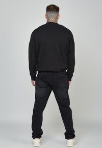 Felpa nera con scollo rotondo, abbinata a jeans in denim scuro. L'outfit è completato da sneakers bianche, che mostrano uno stile casual.