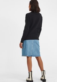 Schwarzer, strukturierter Strickpullover, Jeansrock mit heller Waschung und weiße Knöchelstiefel mit schwarzen Akzenten. Klare Nähte und schlichtes Design.