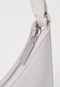 Vaaleanpunainen käsilaukku, joka on valmistettu sileästä nahasta ja jossa on hopeanvärinen vetoketju. Laukku on yksinkertaisen mallinen ja siinä on vetoketjun vetimenä Calvin Kleinin logo.