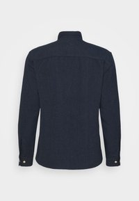 Chemise bleu marine foncé à manches longues avec poignets boutonnés vue de dos sur un fond blanc uni.