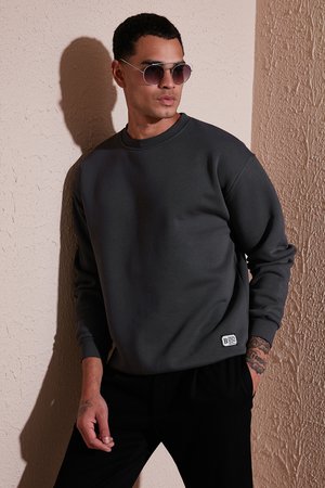 Dark gray sweatshirt featuring a crew neckline, ribbed cuffs, and a small branded label at the hem, paired with round sunglasses.