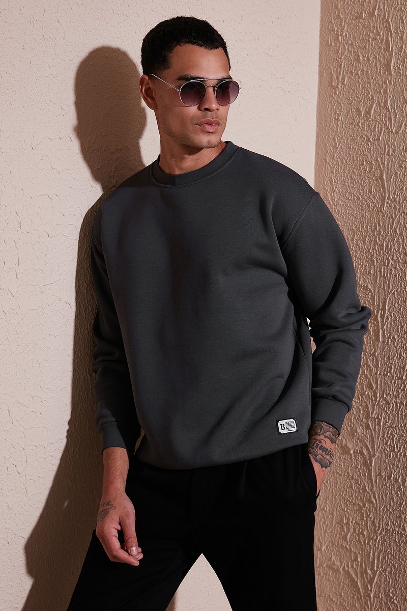 Sudadera gris oscuro con cuello redondo, puños de canalé y una pequeña etiqueta de marca en el dobladillo, combinada con gafas de sol redondas.