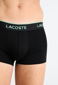 Zwarte boxershorts met een groenaccent in de tailleband, voorzien van het "LACOSTE" logo. Soepele textuur, nauwsluitende pasvorm en een middelhoge snit.