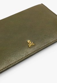 Cartera de cuero verde olivo con un pequeño emblema de calavera dorada y huesos cruzados en la esquina inferior derecha, con textura y costura visibles.