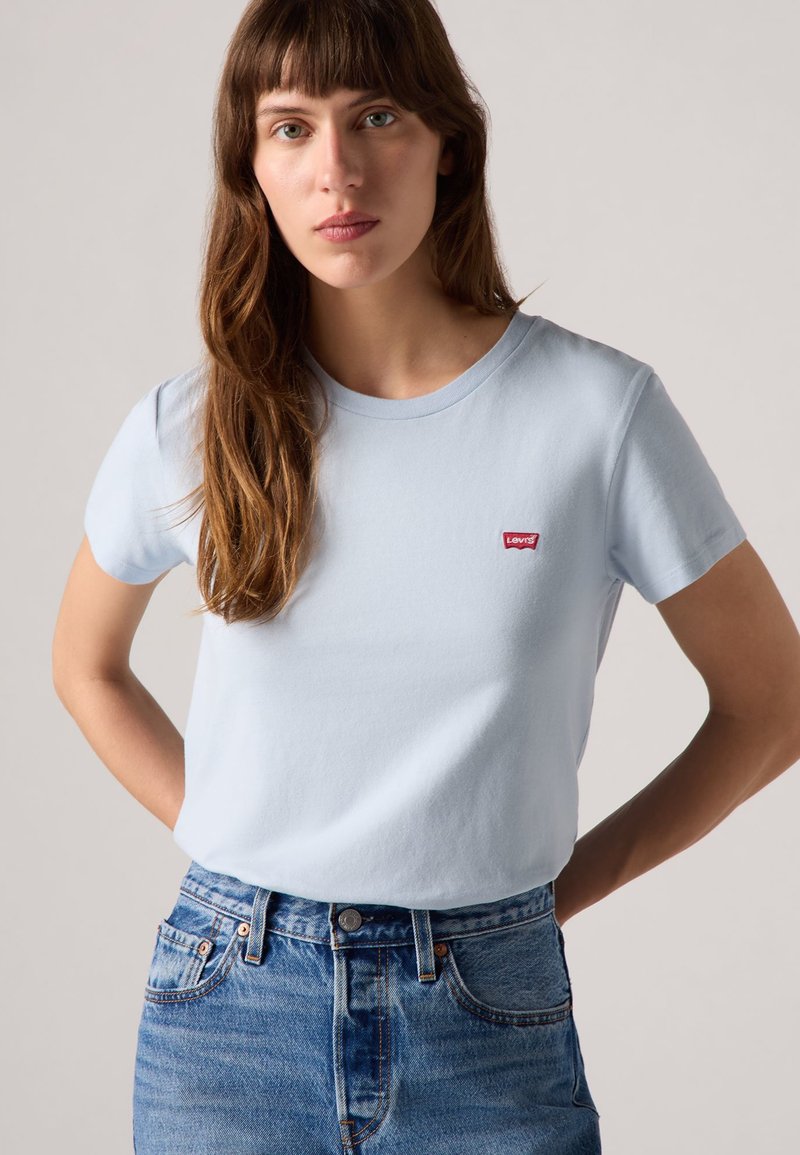 Světle modré tričko s krátkým rukávem vyrobené z jemného materiálu, s červenou nášivkou loga Levi's na hrudi a klasickým kulatým výstřihem.