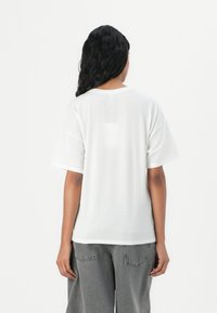 White short-sleeve t-shirt with a round neckline, soft texture, and relaxed fit, paired with gray loose-fitting jeans.