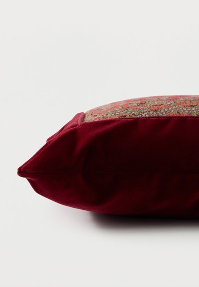 Coussin décoratif rectangulaire avec côtés en velours rouge profond et dessus en tissu à motifs présentant des dessins floraux rouges et dorés complexes.