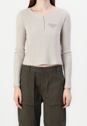 Slim-fit beige ribbet langærmet top med knapper og "Hollister 1981" logo kombineret med højtaljede cargo bukser i olivengrøn.