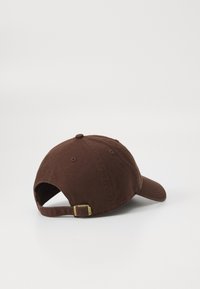Brown cap viewed from the back, featuring a curved brim and an adjustable strap with a metal buckle. Background is plain white.