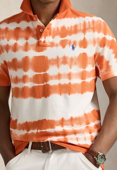 Πόλο μπλούζα σε πορτοκαλί και άσπρο μοτίβο ταϊ-ντάι, με γιακά, τρία κουμπιά και μπλε λογότυπο. Υφασμάτινο βαμβάκι με υφή και άνετη εφαρμογή.