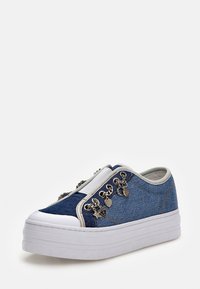 Denim slip-on tennarit, joissa on valkoinen alustaso, koristeltuna hopeanvärisillä charmilla, jotka ovat tähden, sydämen ja logon muotoisia sivussa.