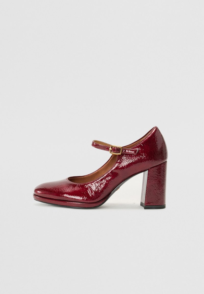 Escarpin Mary Jane en cuir vernis rouge avec un bout rond, une bride de cheville et un talon épais. Texture lisse avec une finition brillante.