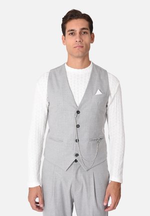 Gilet grigio con tasche frontali, sei bottoni e un dettaglio a catena argentata. Indossato sopra una camicia bianca a maniche lunghe con texture.