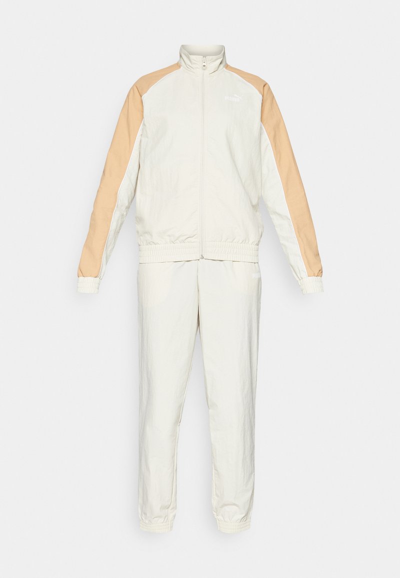 Trainingsanzugset in Creme und Beige. Es besteht aus einer zipfelbaren Jacke mit hohem Kragen, elastischen Bündchen und passenden Hose mit elastischem Bund.