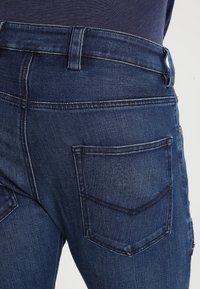 Mörkblå denimjeans med en åtsittande design, bakfickor med snedställda klaffar och kontrasterande sömmar längs lädret.