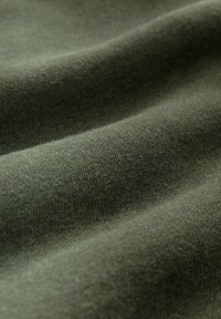 Tessuto verde oliva con una consistenza liscia e morbida. Il materiale presenta leggere ondulazioni, che indicano flessibilità ed elasticità.