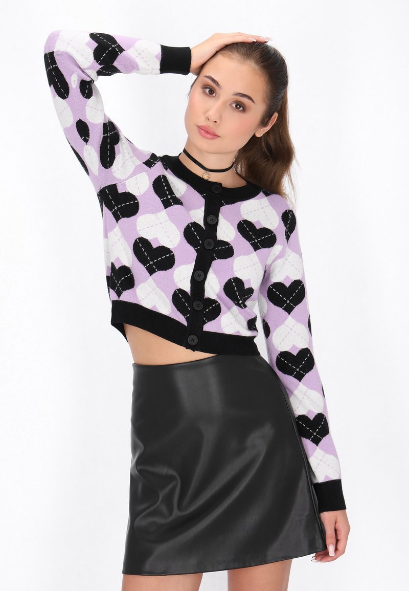 Cardigan all'uncinetto in lilla con motivi a cuori neri, chiusura con bottoni e polsini a coste neri. Abbinato a una mini gonna di pelle nera.
