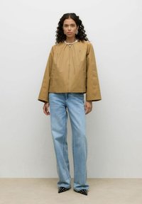 Veste marron raccourcie avec manches évasées, tissu légèrement brillant et encolure ronde, associée à un jean large bleu clair et des chaussures noires pointues.