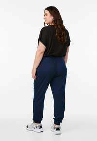 Zwarte T-shirt met korte mouwen, losse pasvorm, gecombineerd met marineblauwe joggers, elastische tailleband en opgerolde enkels. Schoenen zijn grijs met zwarte accenten.